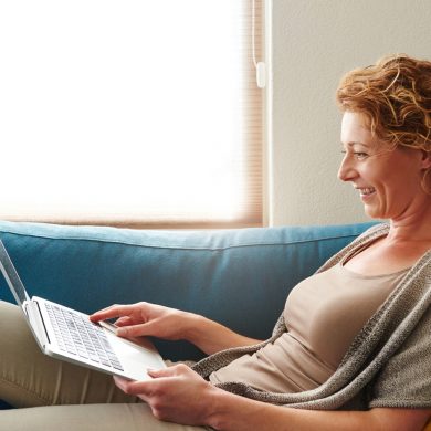 Woman lying on sofa with laptop smiling